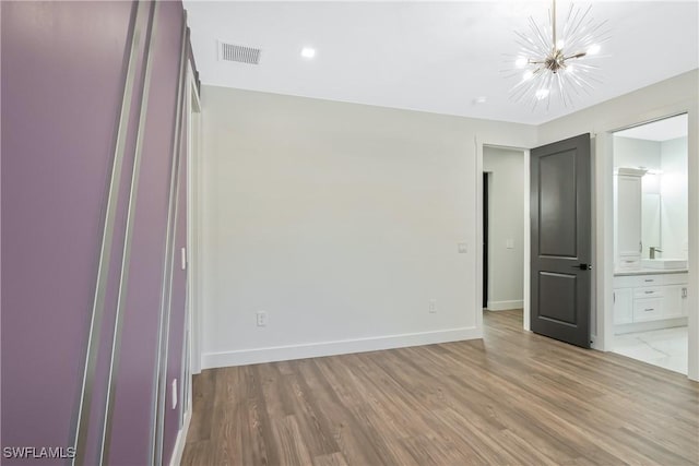 unfurnished bedroom featuring connected bathroom, an inviting chandelier, and light hardwood / wood-style flooring