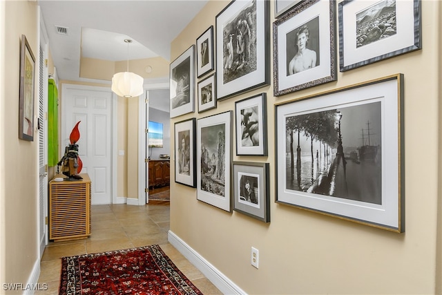 corridor featuring baseboards, visible vents, a tray ceiling, and tile patterned floors