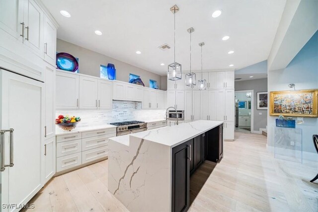 kitchen featuring a large island, white cabinets, hanging light fixtures, light wood-type flooring, and high end range