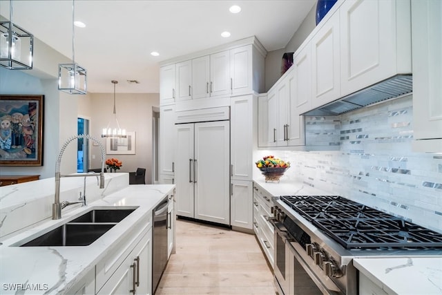 kitchen featuring premium appliances, sink, light wood-type flooring, white cabinetry, and decorative light fixtures