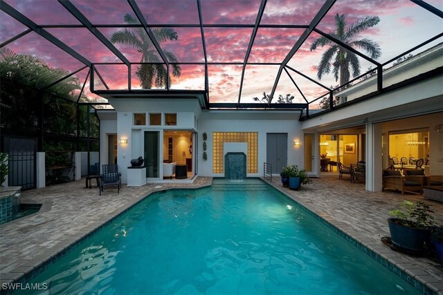 pool at dusk featuring a patio and glass enclosure