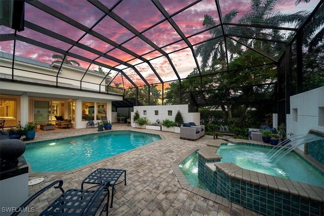 pool at dusk featuring an in ground hot tub, pool water feature, a patio area, and a lanai