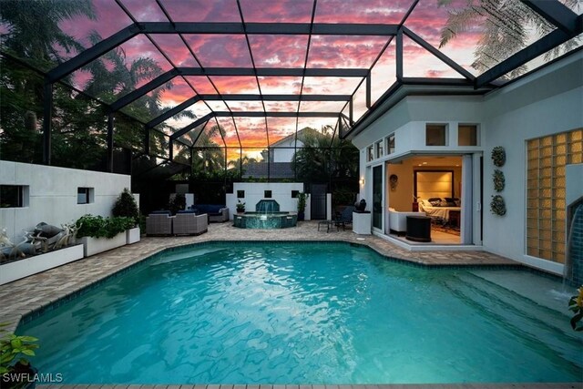 pool at dusk with a patio, a hot tub, and glass enclosure