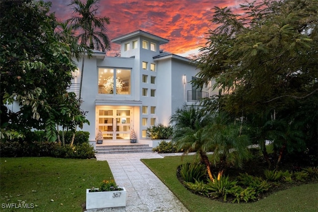 back house at dusk with french doors and a lawn