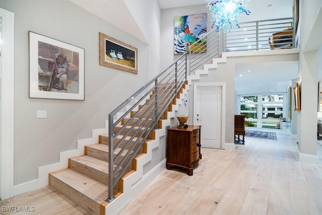 staircase featuring a chandelier, wood-type flooring, and a high ceiling