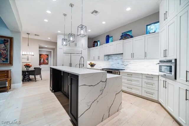 kitchen with a center island with sink, pendant lighting, white cabinets, and stainless steel appliances