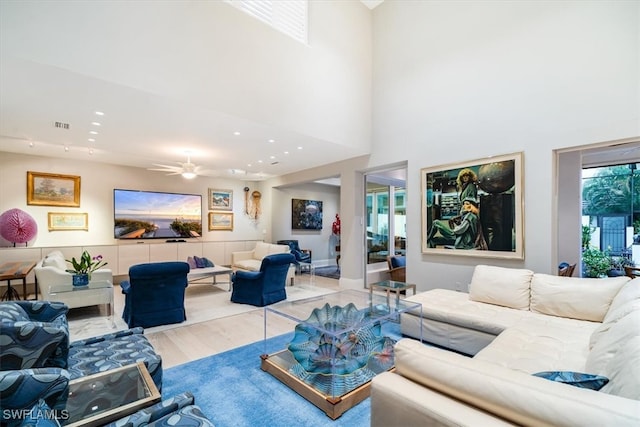 living room with light hardwood / wood-style floors, a towering ceiling, and ceiling fan