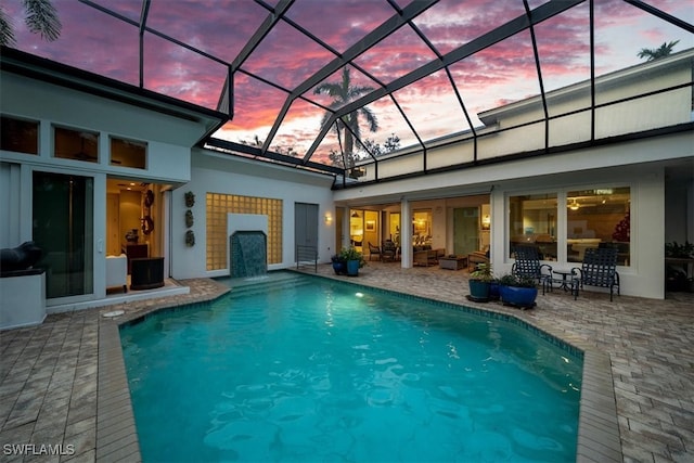 pool at dusk featuring a patio area and glass enclosure