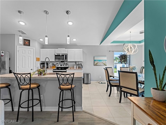 kitchen featuring decorative light fixtures, vaulted ceiling, a notable chandelier, stainless steel appliances, and white cabinets