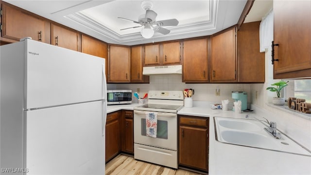 kitchen with white appliances, sink, a tray ceiling, crown molding, and light hardwood / wood-style flooring