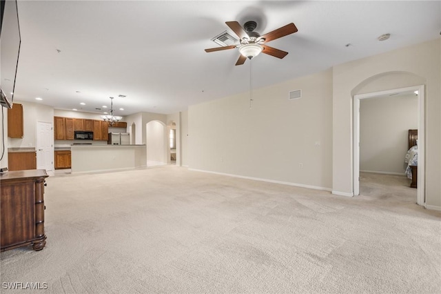 unfurnished living room featuring ceiling fan with notable chandelier and light colored carpet