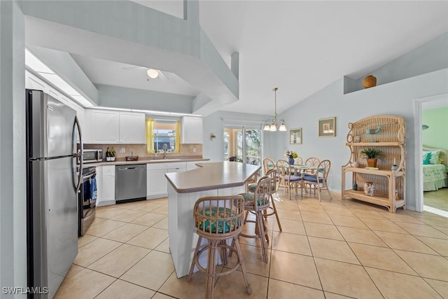 kitchen featuring hanging light fixtures, white cabinets, light tile patterned floors, decorative backsplash, and stainless steel appliances