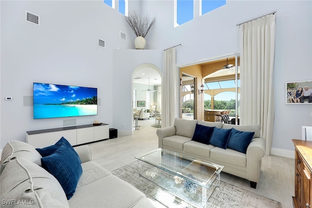 living room with a towering ceiling, ceiling fan, and light hardwood / wood-style flooring