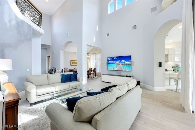 living room featuring ornamental molding, light wood-type flooring, and a high ceiling