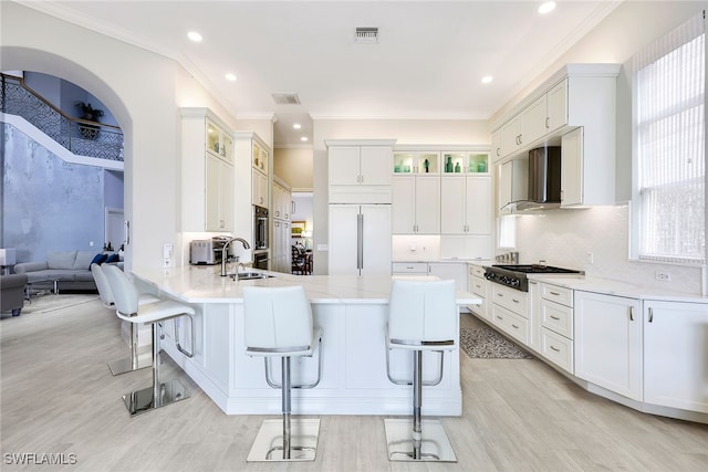 kitchen with white cabinetry, a kitchen breakfast bar, stainless steel appliances, and wall chimney range hood