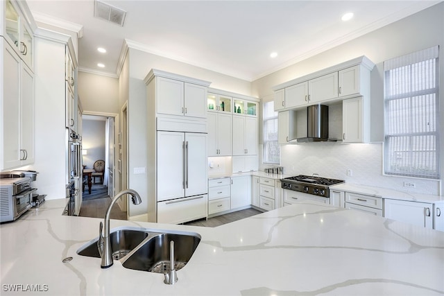 kitchen featuring paneled refrigerator, white cabinetry, light stone counters, and wall chimney exhaust hood