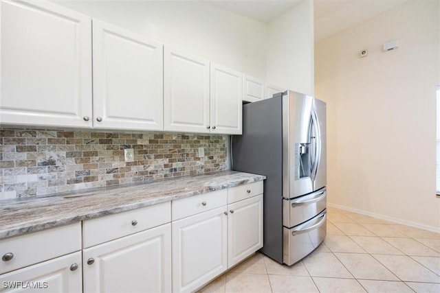 kitchen with light stone countertops, light tile patterned floors, stainless steel refrigerator with ice dispenser, backsplash, and white cabinetry