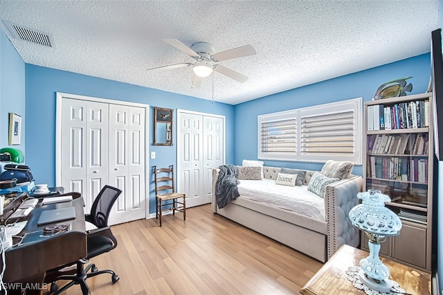 bedroom with ceiling fan, a textured ceiling, light wood-type flooring, and two closets