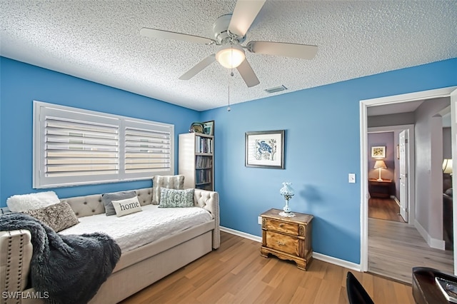 bedroom featuring light hardwood / wood-style floors, a textured ceiling, and ceiling fan