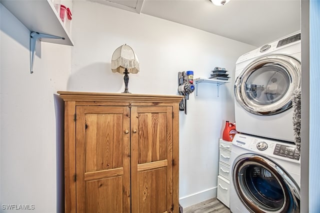 laundry area featuring stacked washer / dryer, cabinets, and light wood-type flooring