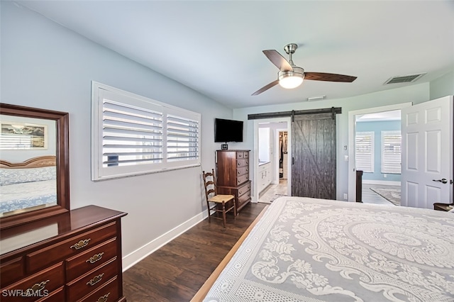 bedroom with a barn door, dark hardwood / wood-style floors, and ceiling fan