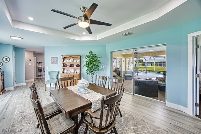 dining area featuring ceiling fan, a tray ceiling, and light hardwood / wood-style flooring