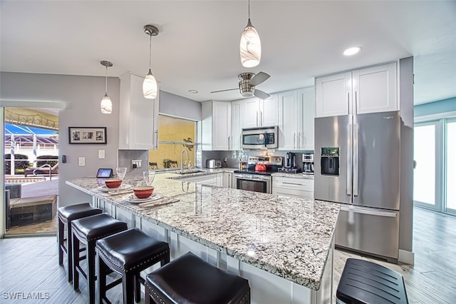 kitchen featuring light hardwood / wood-style flooring, backsplash, pendant lighting, white cabinetry, and appliances with stainless steel finishes