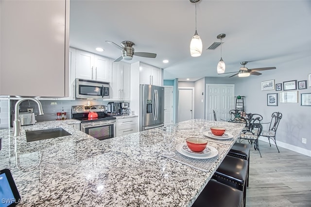 kitchen with light stone countertops, sink, white cabinetry, light hardwood / wood-style floors, and stainless steel appliances