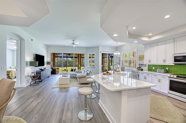 kitchen featuring stainless steel appliances, white cabinetry, ceiling fan, backsplash, and hanging light fixtures