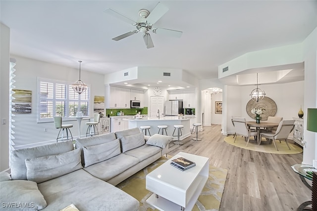 living room featuring ceiling fan with notable chandelier and light hardwood / wood-style floors