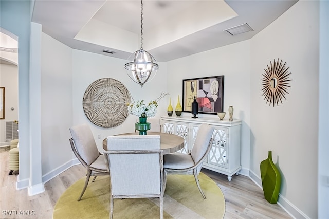 dining room with a notable chandelier, light wood-type flooring, and a tray ceiling