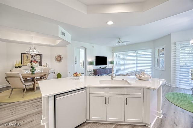 kitchen featuring decorative light fixtures, sink, dishwashing machine, white cabinets, and a raised ceiling