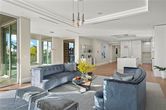 living room with a tray ceiling, sink, and light wood-type flooring