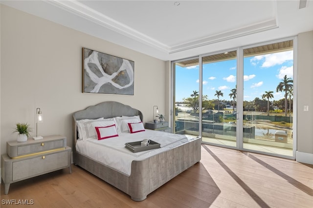 bedroom with expansive windows, light hardwood / wood-style floors, a water view, and access to outside