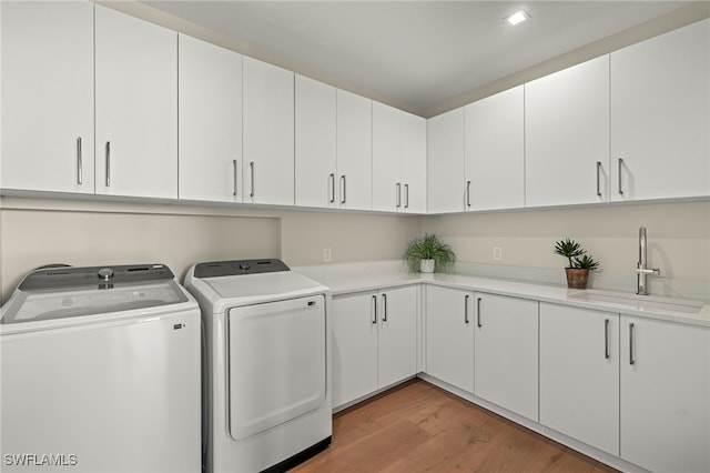 clothes washing area featuring independent washer and dryer, cabinets, light wood-type flooring, and sink