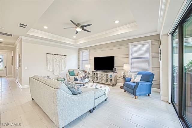 living room featuring ornamental molding, a tray ceiling, plenty of natural light, and ceiling fan