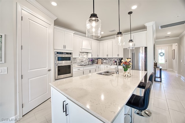 kitchen with sink, an island with sink, hanging light fixtures, and white cabinetry