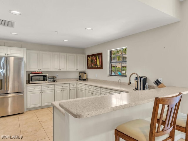 kitchen with appliances with stainless steel finishes, kitchen peninsula, a kitchen bar, and white cabinets