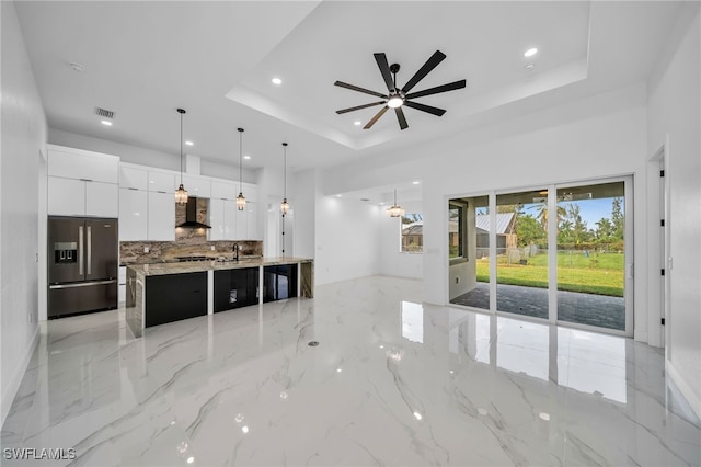 kitchen featuring a spacious island, wall chimney range hood, stainless steel fridge with ice dispenser, decorative light fixtures, and white cabinets