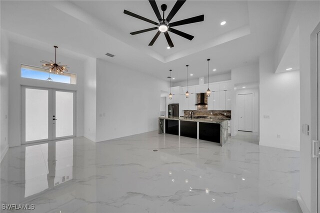 kitchen with wall chimney range hood, hanging light fixtures, a large island, stainless steel fridge, and white cabinetry