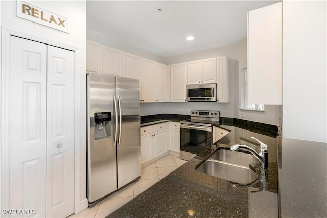 kitchen with sink, light tile patterned flooring, dark stone countertops, white cabinets, and appliances with stainless steel finishes