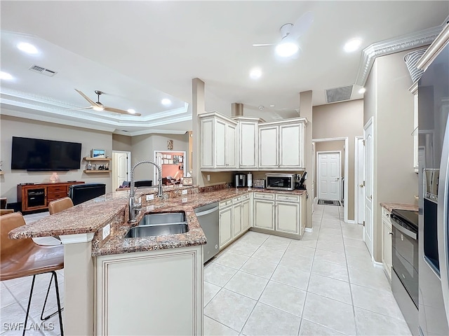 kitchen with sink, stainless steel appliances, a raised ceiling, kitchen peninsula, and a breakfast bar area