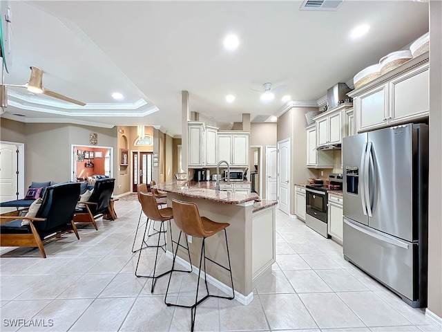 kitchen with a kitchen breakfast bar, light stone counters, a tray ceiling, appliances with stainless steel finishes, and ornamental molding