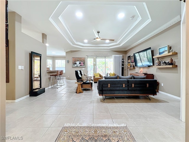 tiled living room with a raised ceiling, ceiling fan, and ornamental molding