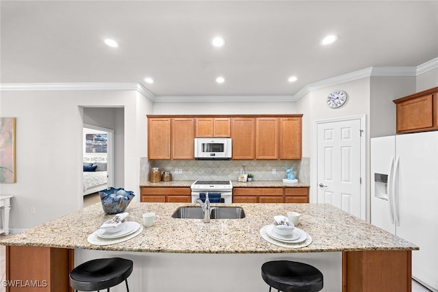 kitchen featuring a kitchen island with sink, a kitchen breakfast bar, ornamental molding, light stone countertops, and white appliances