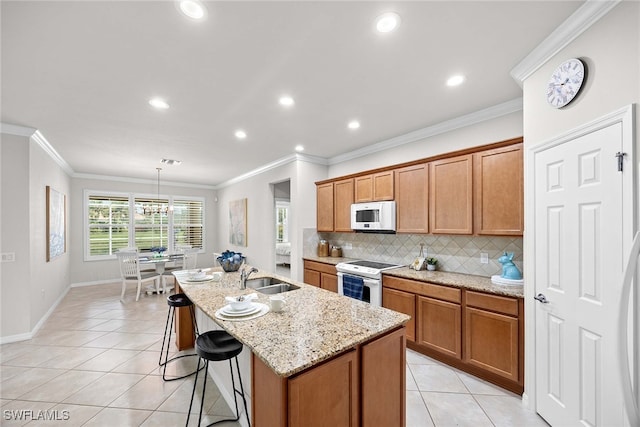 kitchen featuring a center island with sink, light tile patterned floors, ornamental molding, pendant lighting, and white appliances