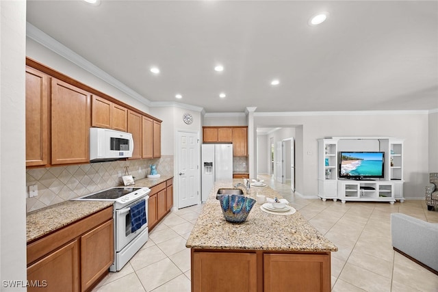 kitchen featuring an island with sink, light stone countertops, crown molding, and white appliances