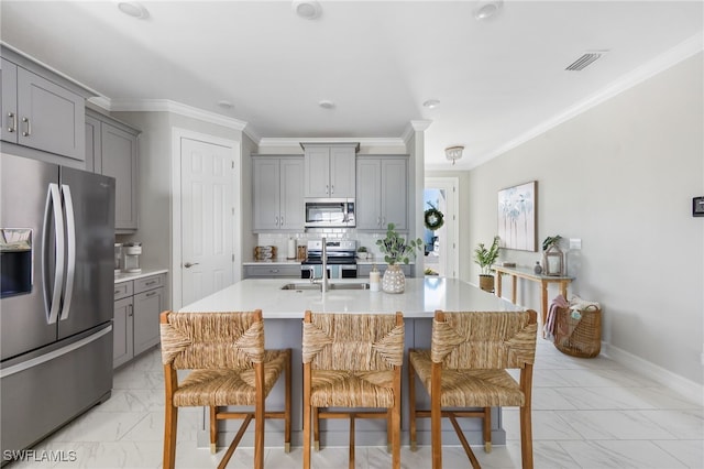 kitchen with gray cabinetry, tasteful backsplash, an island with sink, stainless steel appliances, and ornamental molding