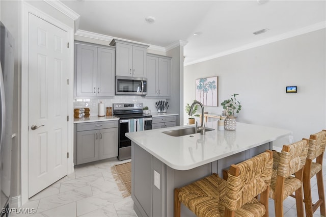 kitchen with a center island with sink, a kitchen breakfast bar, ornamental molding, sink, and stainless steel appliances