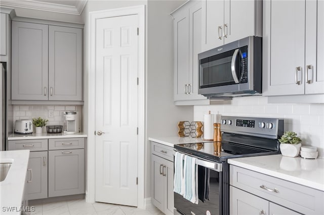 kitchen with backsplash, appliances with stainless steel finishes, gray cabinets, crown molding, and light stone counters